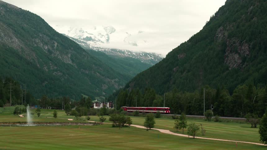 Landscape of a greenish mountain valley with a red train passing by