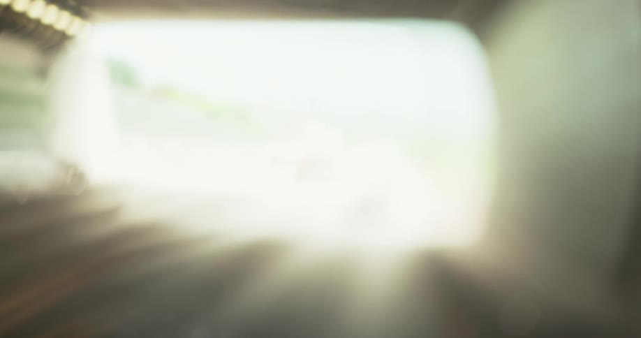 A blurry view of traffic lights car headlights and the inside of a tunnel is shown eventually becoming totally out of focus to white
