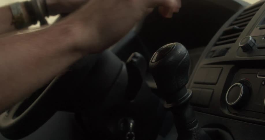 A hand adorned with ornate rings grips the steering wheel and gear shift while driving
