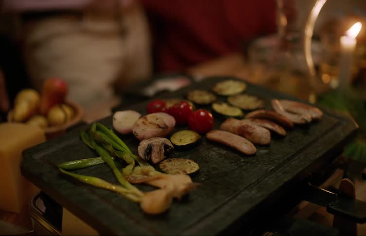 People sitting at a table and a hot plate with roasted vegetables and proteins
