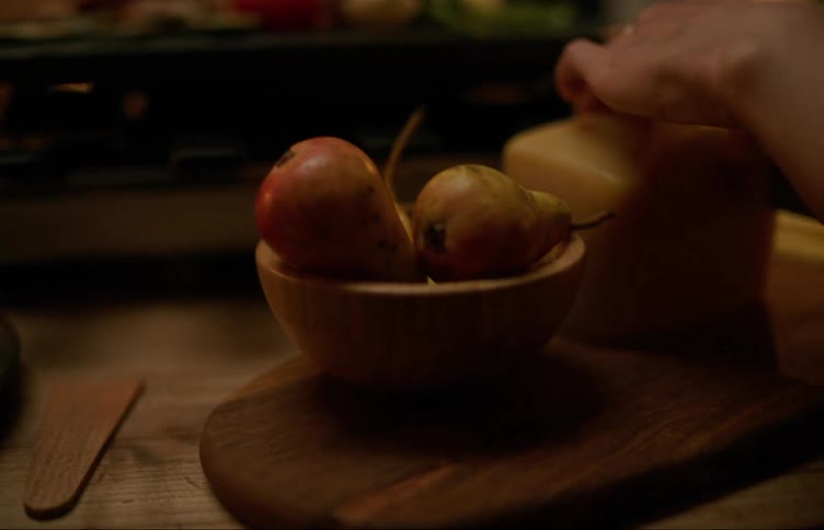 A woman slices a block of cheese that sits next to a bowl of pears