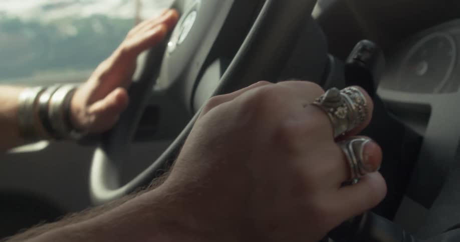 A person drives a car with a mountainous landscape visible through the windshield