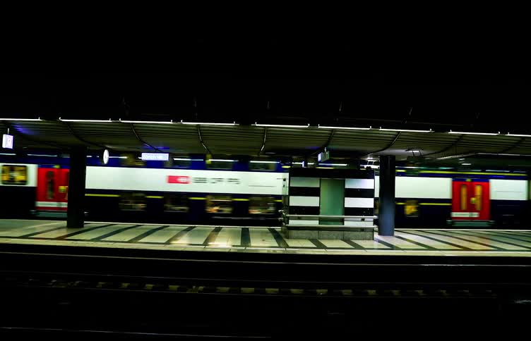 A passenger train streaks past a dimly lit station platform its vibrant colors blurring into streaks of motion