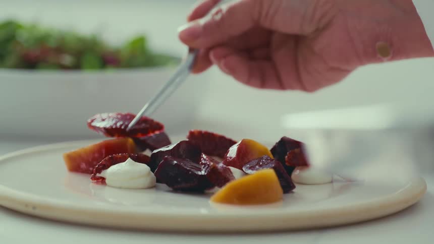 A hand is delicately placing a piece of food on a plate with tweezers arranging a dish