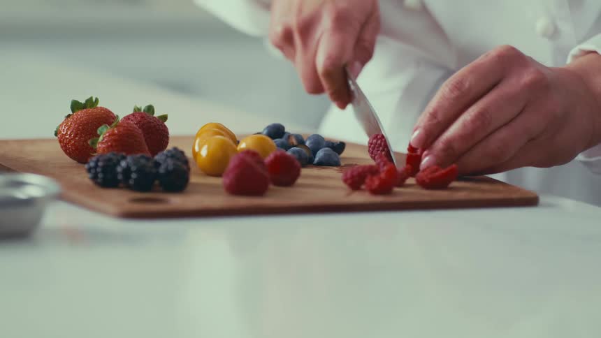 A chef carefully slicing a variety of fresh berries on a wooden cutting board