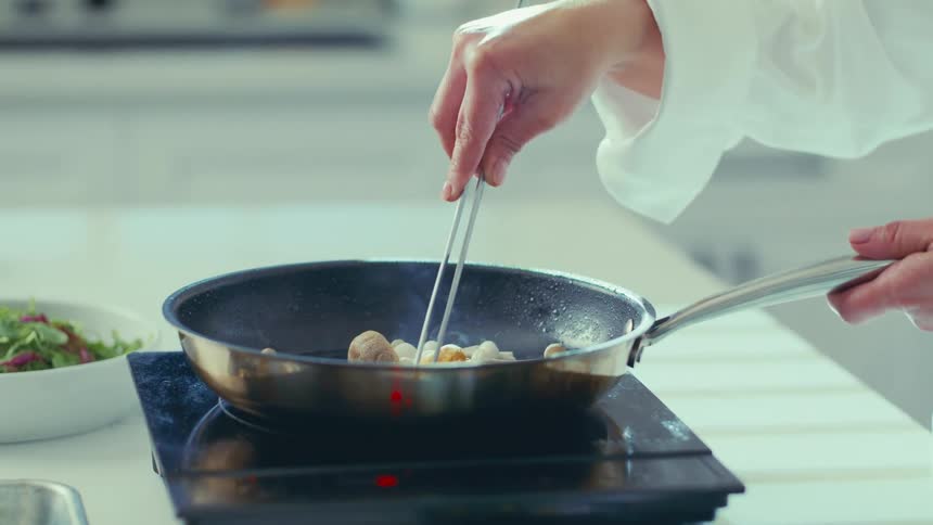 A chef in a white uniform cooking in a pan on a stovetop in the kitchen