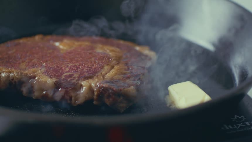 Butter is dropped onto a skillet with a sizzling steak