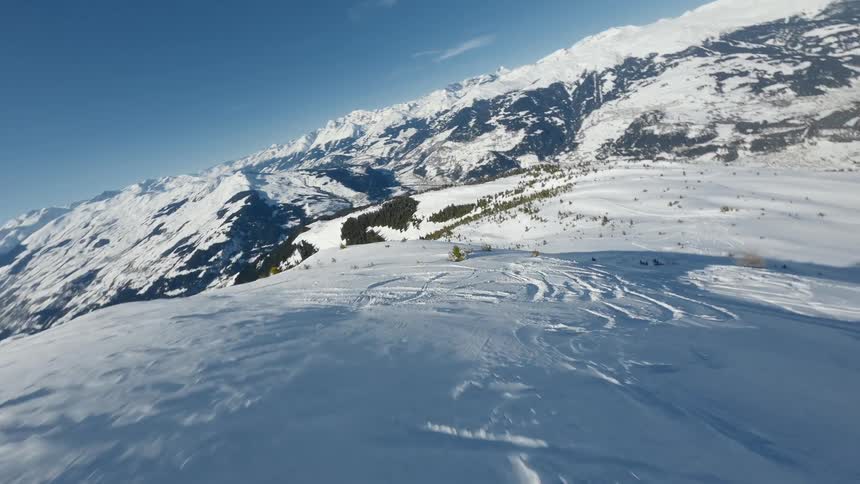 Drone moving over a snow covered mountain slope with trees and mountains in the distance