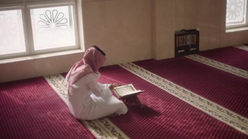 Arab person sitting on the floor on a carpet in a religious dome reading a book
