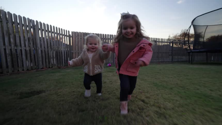 Two little girls running in a grassy yard