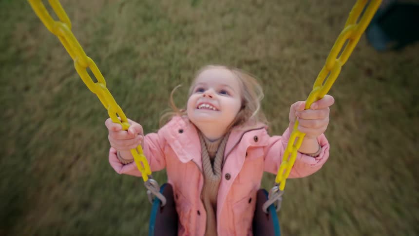 A person pushes a young girl on a swing at sunset