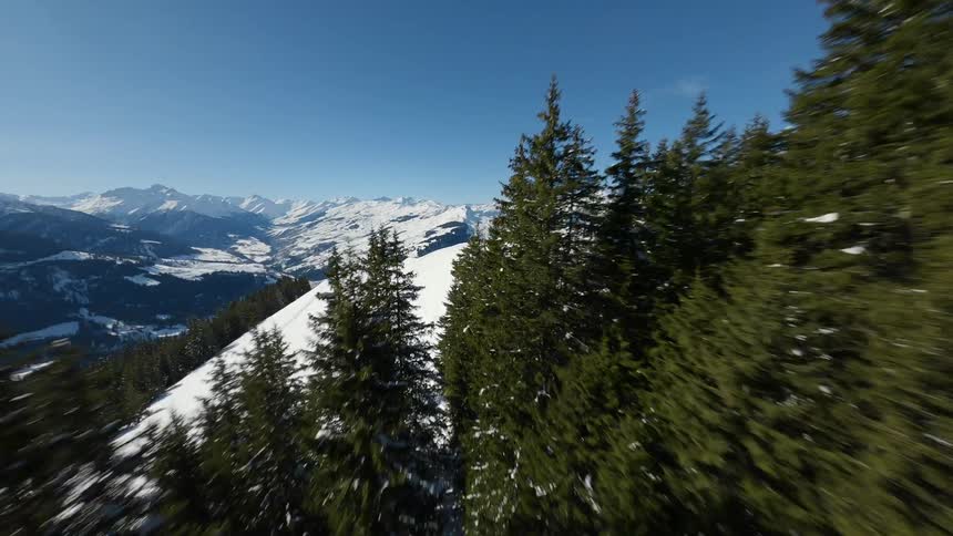 FPV drone flies through trees and over snow covered mountains under a clear sky in Switzerland