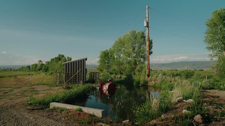 Small lake in a green field with mountains in the background