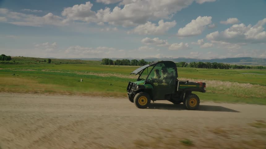 A man is riding in a John Deere quad with his dog