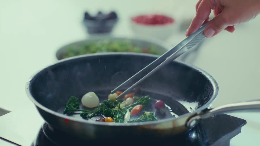 Hand with tongs cooking vegetables in a frying pan