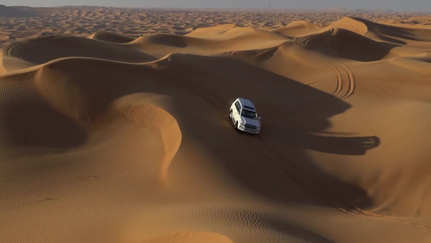 Sunlight shines upon a van driving on desert dunes and sliding down