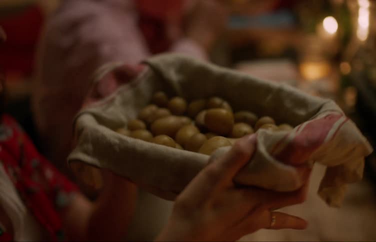 Person passing baked potatoes to another on a table at night