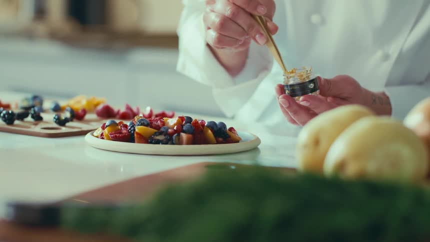 A chef carefully garnishes a plate of colorful fruit salad