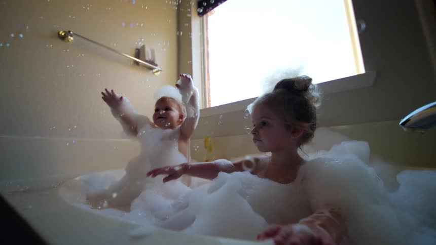 A girl is taking a bubble bath with a baby at home