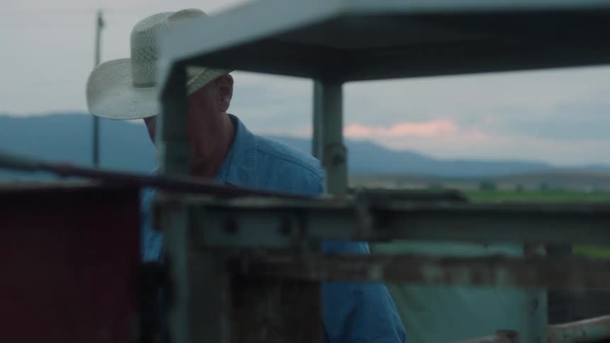 A man wearing a blue shirt and a cowboy hat walks around a corral on a ranch