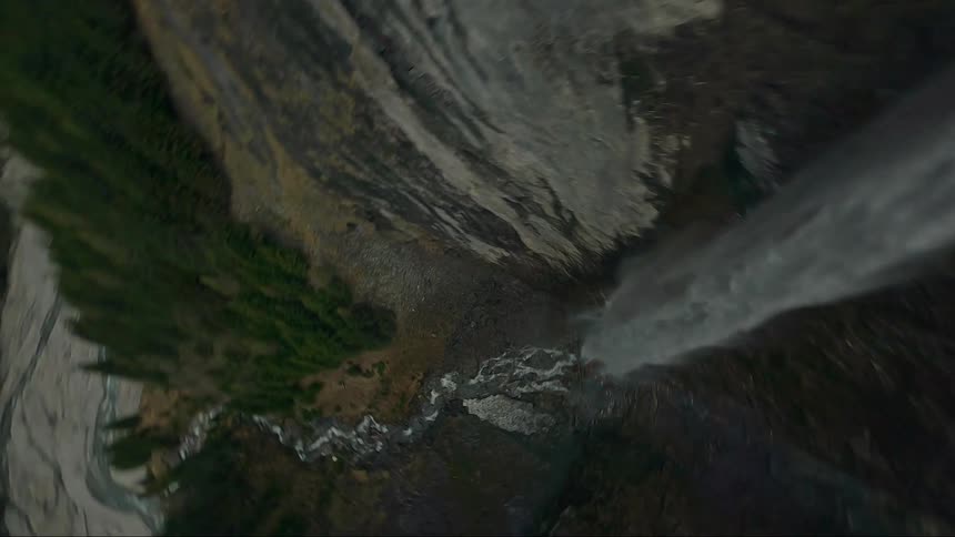An aerial view of a powerful waterfall cascading down a sheer cliff face with the water appearing almost white against the dark rock