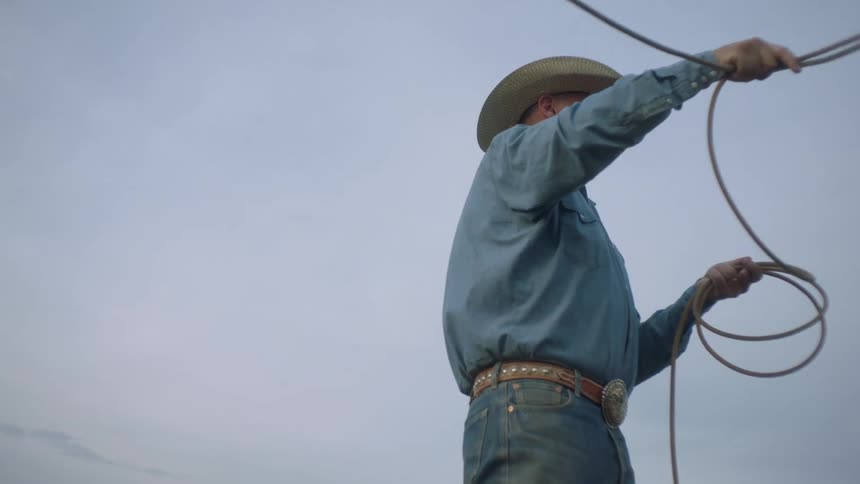 A cowboy swings a lasso above his head