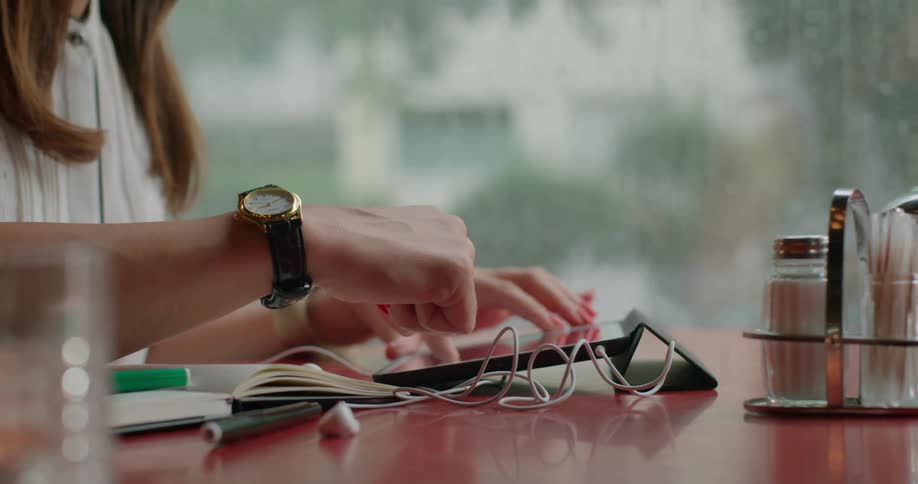 Pair of hands interacting with a tablet on a table and then picking up a mug
