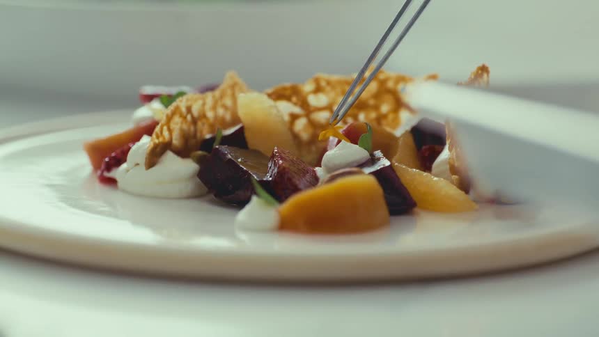 Tweezers finishing a plate with vegetables and fruits
