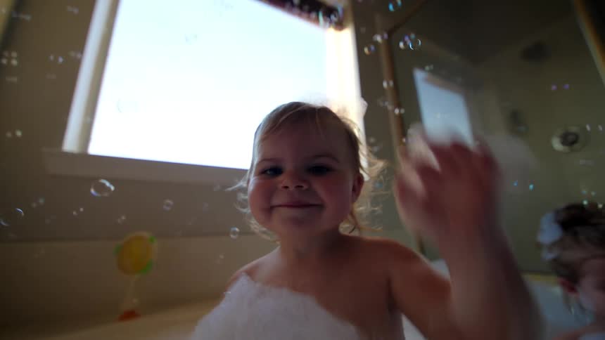 Two smiling children bathe in a bathtub full of foam surrounded by bubbles floating in the air