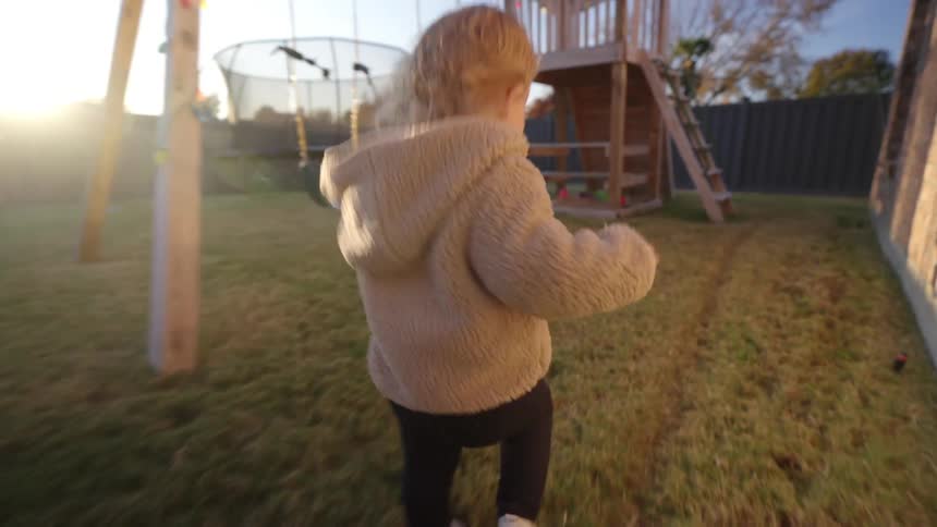 A child runs around a play area in the backyard in the morning