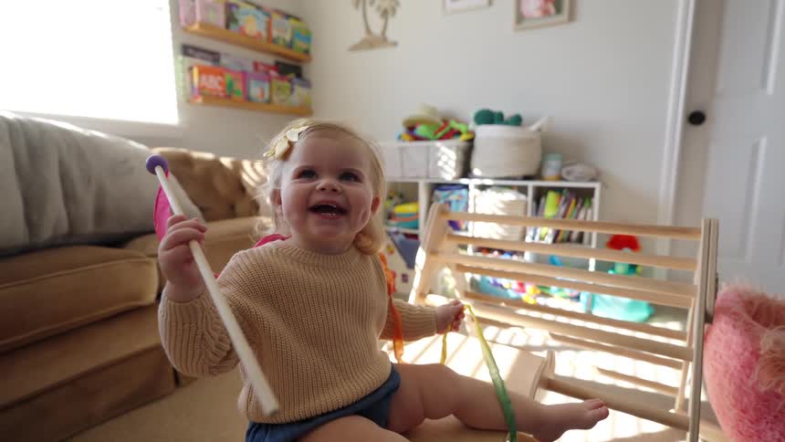 Girl sitting in the living room plays with a stick holding a colorful ribbon