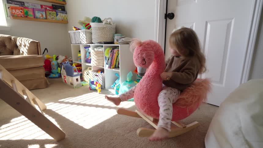 A child is joyfully swinging on a pink flamingo in a room filled with various toys and a cozy atmosphere