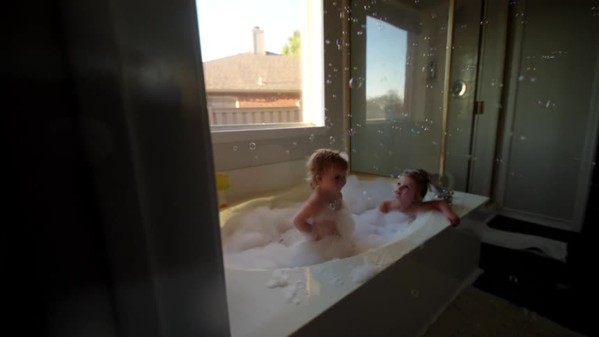 Two little girls playing in a bathtub with foam and soap bubbles