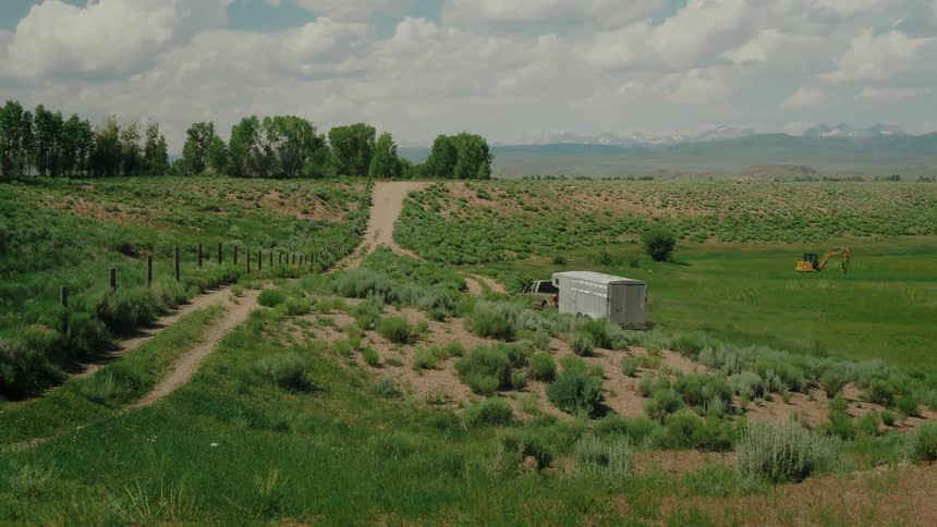 A pickup truck towing a horse trailer parked on a dirt road in a rural landscape with mountains in the distance