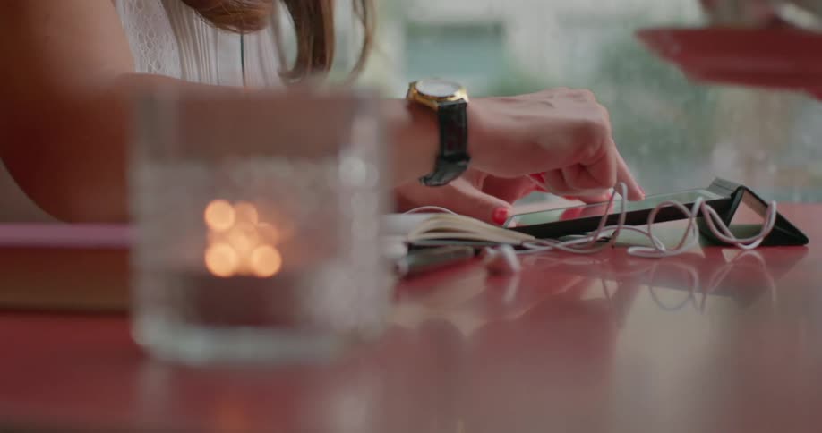 Woman using a tablet device while sitting at a table with a cup of coffee and a notebook
