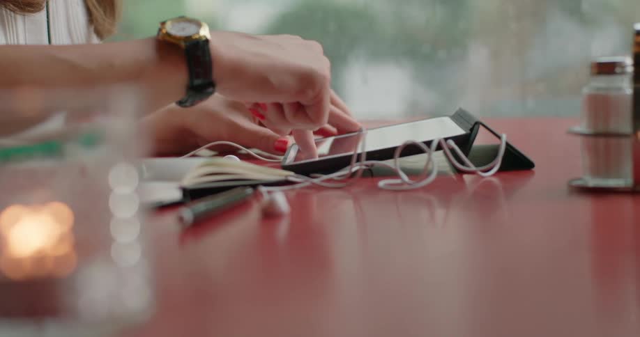 A woman using a tablet device while sitting at a table with a cup of coffee enjoying a quiet moment indoors on a rainy day