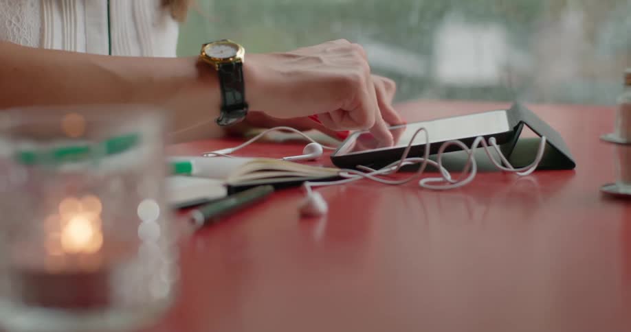 A waiter places a cup of coffee on a cafe table in front of a woman wearing a wristwatch and using her tablet