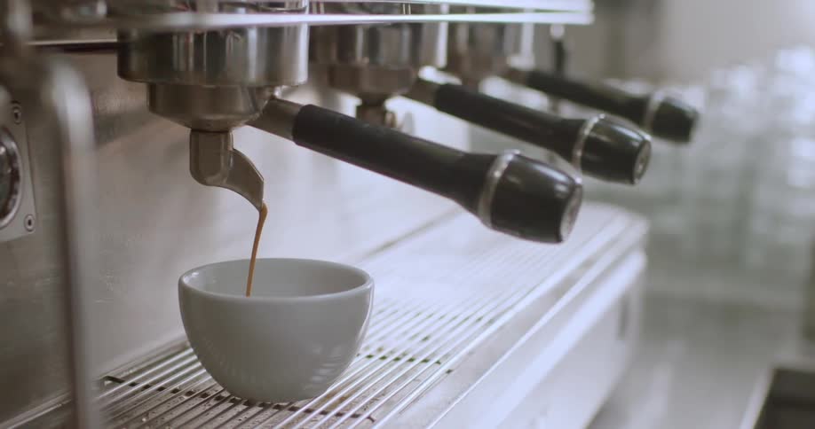 A professional espresso machine is brewing a shot of espresso with the dark liquid flowing into a small white cup