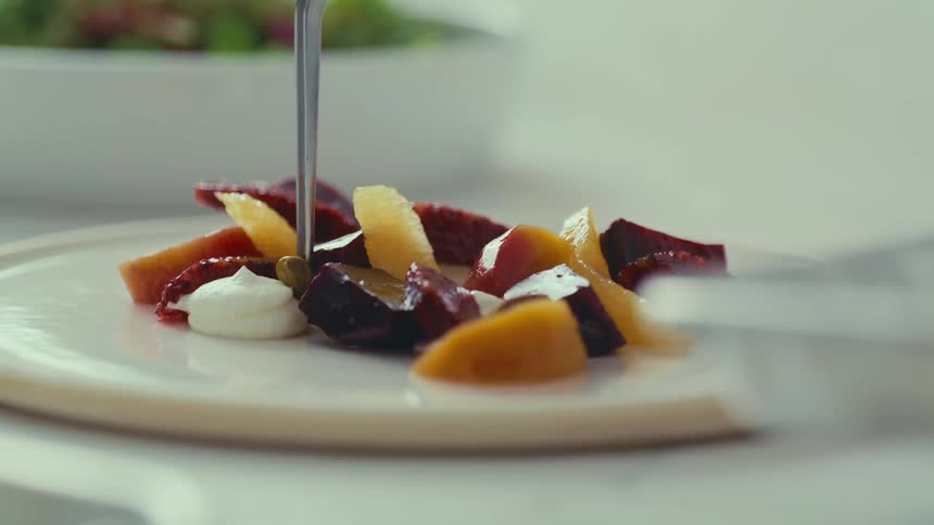 A hand carefully adds a finishing touch to a plate of vibrant beet and fruit salad