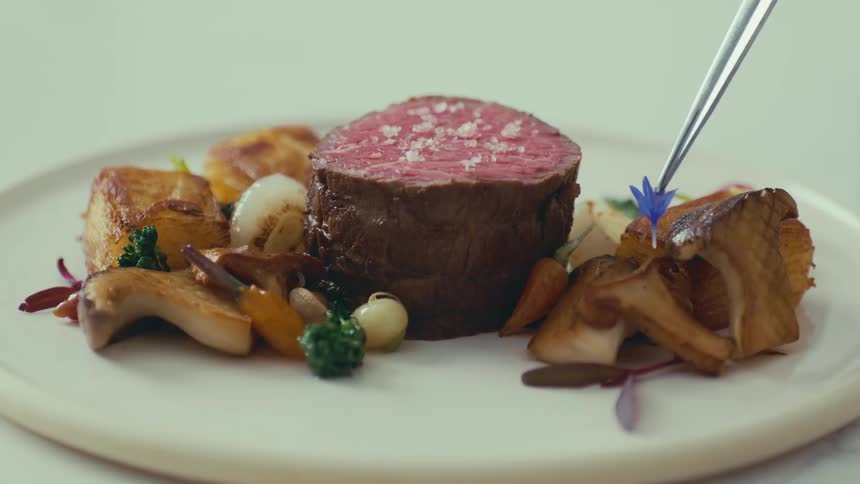 A purple flower garnish is placed on top of a plate of sauteed mushrooms with filet mignon