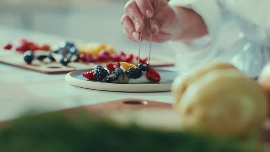 A hand carefully arranges an assortment of berries and fruit slices on a plate creating a colorful and appetizing display