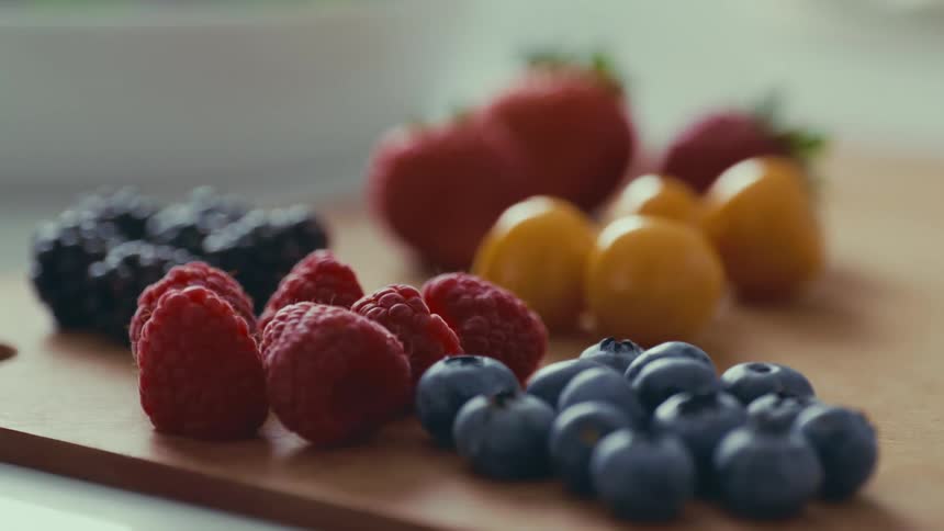 A variety of colorful berries arranged on a wooden cutting board including strawberries raspberries blackberries and blueberries