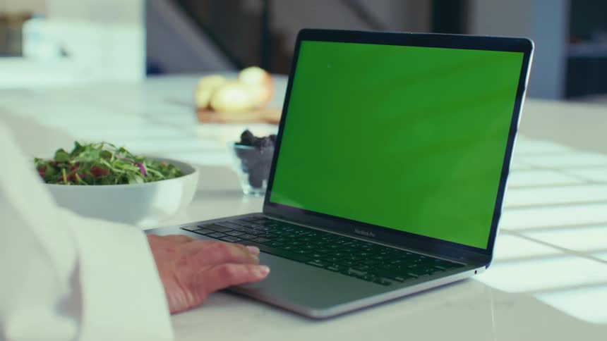 Hand interacting with an open laptop on a kitchen counter