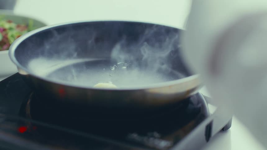 Hand pouring butter into a heated frying pan