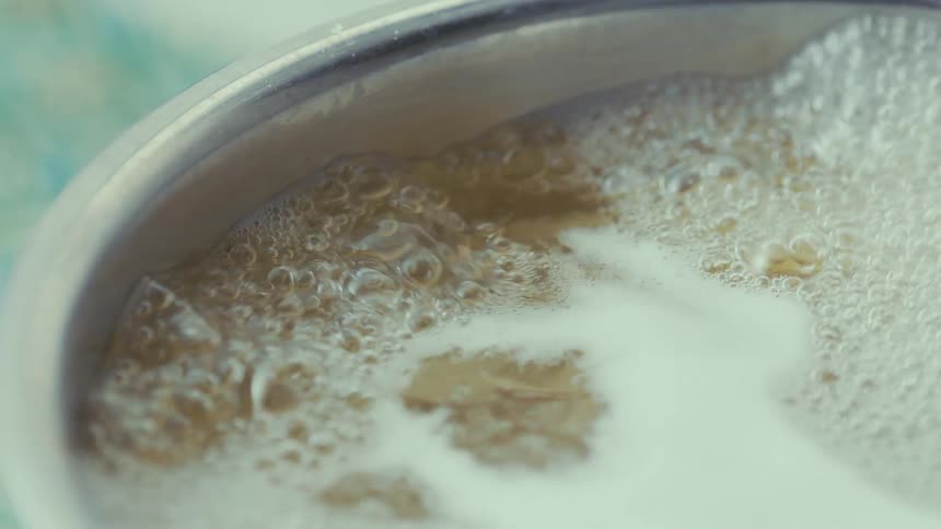 A pot filled with a golden liquid vigorously bubbling and releasing steam as strands of pasta cook within