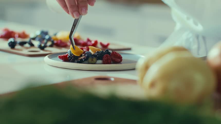 A chef is plating food with a set of tweezers