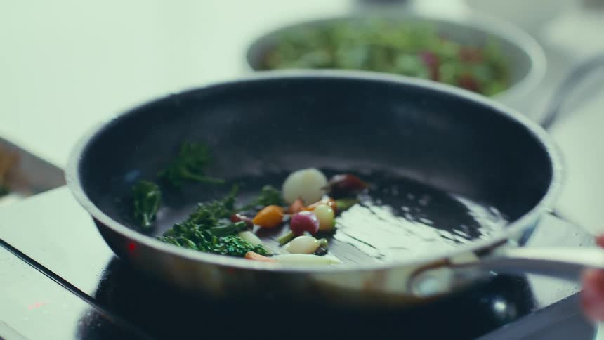A pan filled with a vibrant assortment of colorful vegetables sits on a stovetop being cooked