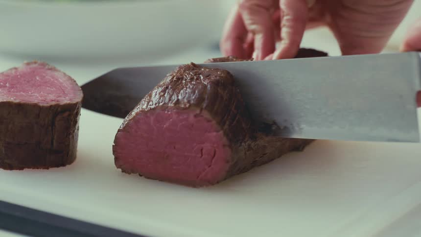 Hand with a knife cutting slices of roast beef
