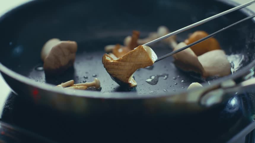 A mushroom is being flipped in a pan with tongs
