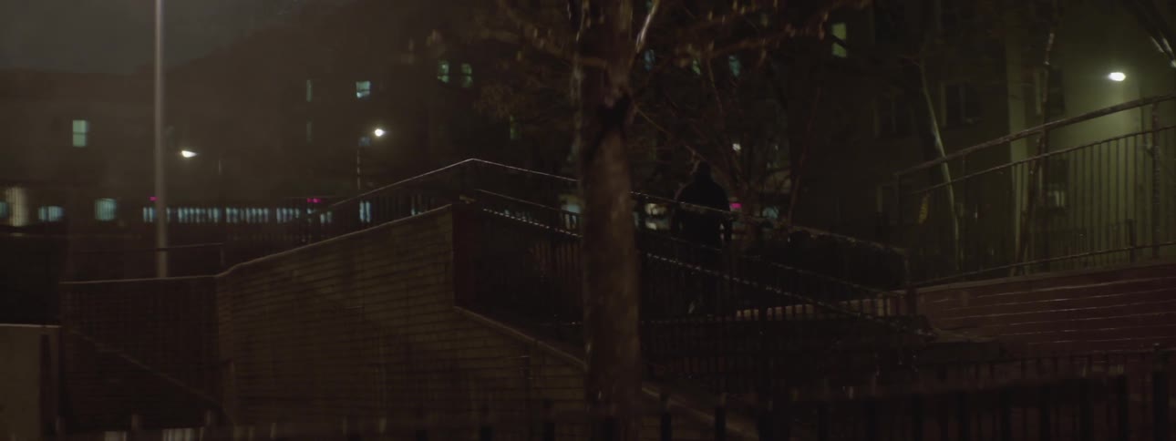 A man is walking up some city stairs at night while a subway train goes past
